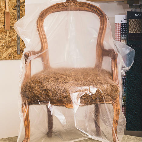 Fauteuil cabriolet ancien en bois doré, assise en crin usée, protégé sous housse plastique avant restauration